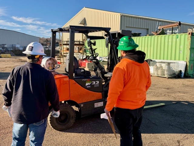 Two people standing next to a forklift